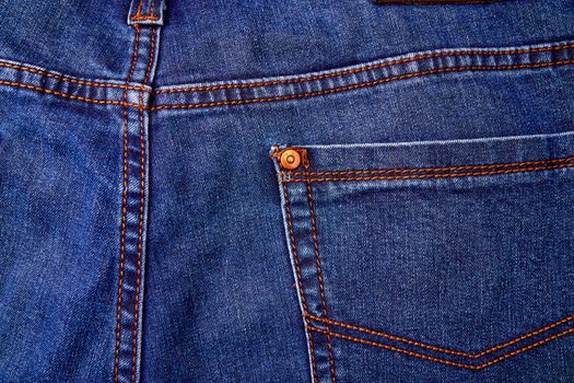 Blue denim jeans background pocket with seam and orange thread stitches.