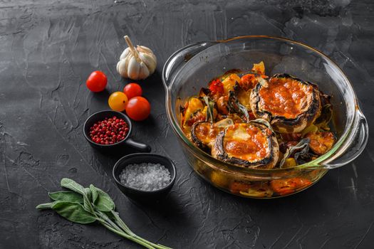 Portobello mushrooms,baked with ingredients cheddar cheese, cherry tomatoes and sage in glass pot on black stone background side view space for text.