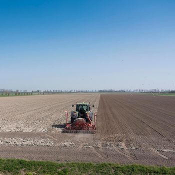 farmer works his land on rural countryside of noord beveland in dutch province zeeland on sunny spring day