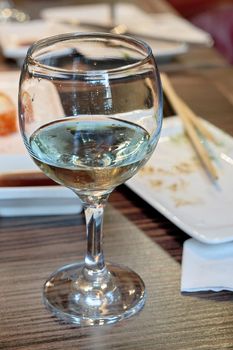 Glass with leftover white wine on the background of table with Japanese cuisine