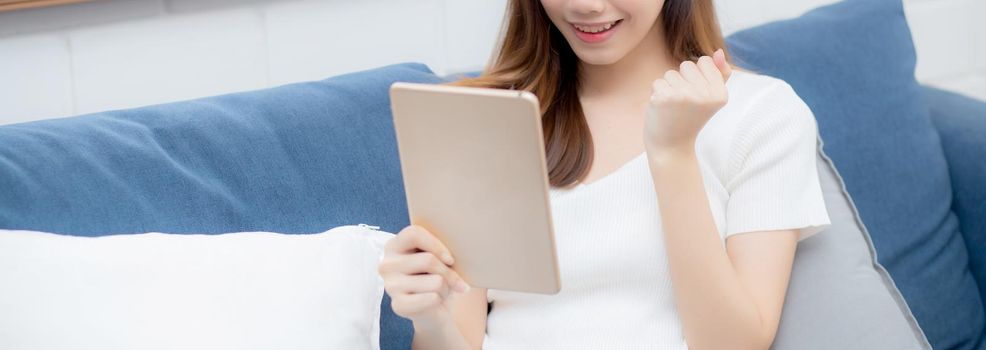 Young attractive asian woman resting using browsing tablet computer on sofa at home, happy girl sitting on couch relax reading digital gadget with excited at house, communication and lifestyle concept.