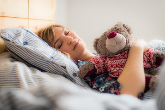 Restful sleep: Young female is sleeping in her bed, teddy bear