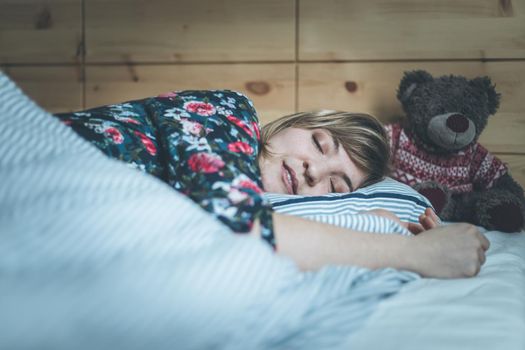 Restful sleep: Young female is sleeping in her bed, teddy bear