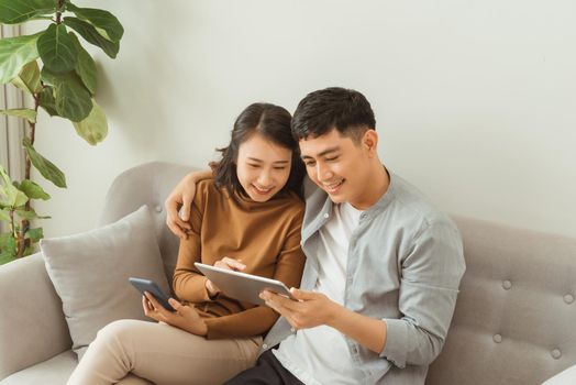 Young couple using a tablet and mobile phone on the couch while enjoying leisure time at home