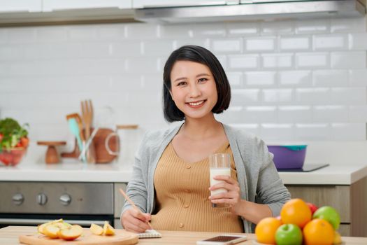 Pregnant woman holding glass milk expectant mother posing in kitchen