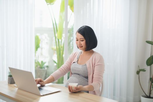 Pregnant positive woman eating jogurt in the livingroom