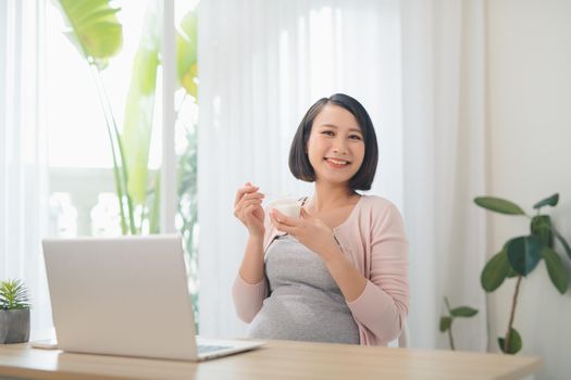 Pregnant positive woman eating jogurt in the livingroom