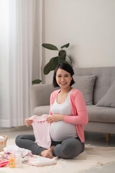 Beautiful pregnant asian woman packing and preparing baby clothes in basket for expectant new born baby
