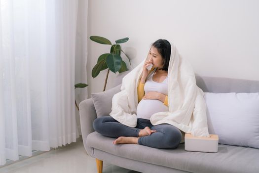 Attractive pregnant woman suffering from cold and flu while sitting on sofa against wall