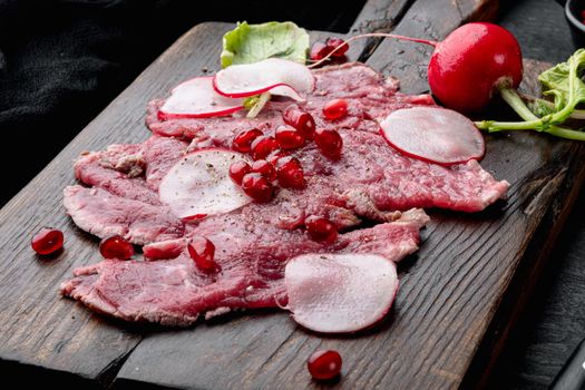 Beef Carpaccio cold appetizer, with Radish and garnet, on wooden serving board, on black wooden table background