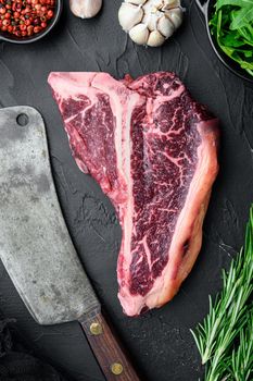Dry-aged Raw T-bone or porterhouse beef meat Steak with herbs and salt, on black stone background, top view flat lay