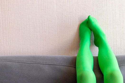 Legs up with green pantyhose resting on the wall and sofa