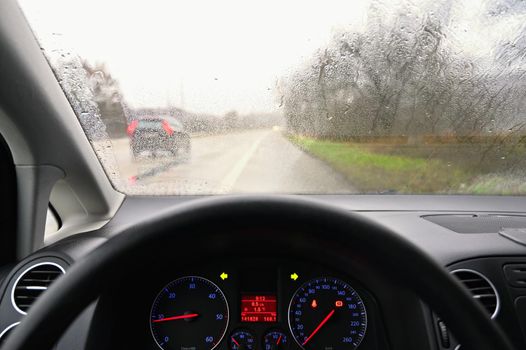 View from the driver - car interior with steering wheel and dashboard. Winter bad rainy weather and dangerous driving on the road.