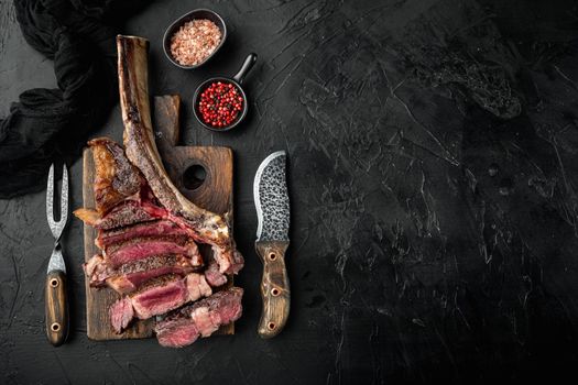 Sliced barbecued tomahawk rib tip with rosemary, salt and herbs medium rare, on wooden serving board, on black stone background, top view flat lay, with copy space for text