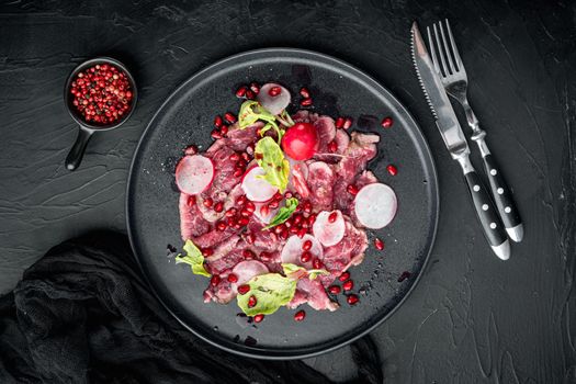 Carpaccio beef, with Radish and garnet, on plate, on black stone background, top view flat lay