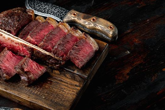 T bone steak is grilled sliced on a piece. Aged Barbecue Porterhouse Steak, on wooden serving board, on old dark wooden table background, with copy space for text