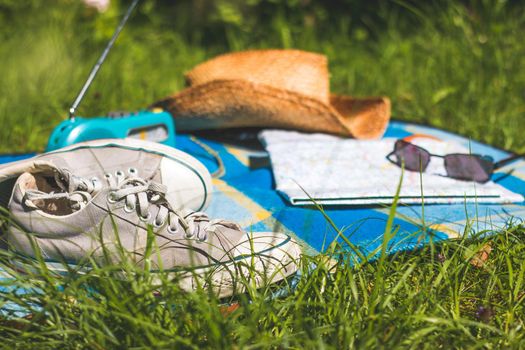 Chilling in the summer concept: picnic blanket with sneakers, straw hat, map and radio