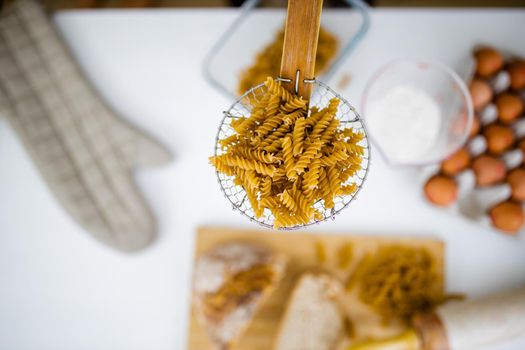Uncooked fusilli on wooden pasta strainer above ingredients on a table