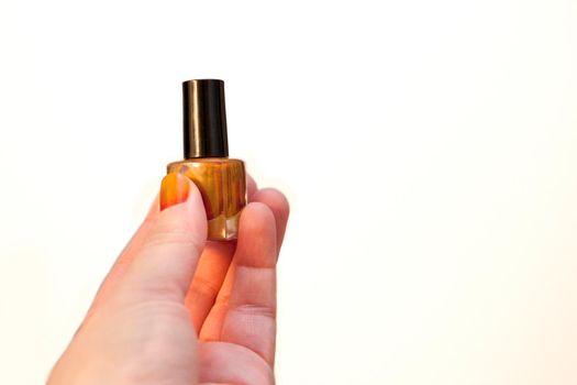 Hand holds bottle of orange nail polish 