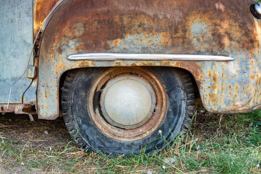 Rear wheel of a rusty vintage american car staying on the grass