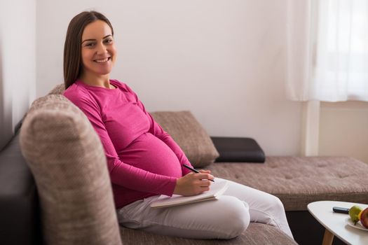 Pregnant woman writing to do list in notebook