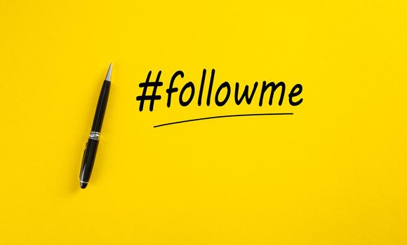 The word follow me or hashtag followme hand written with a black marker pen on yellow background.