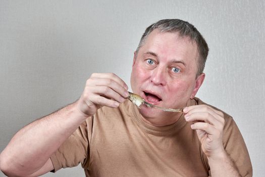 Man eating fried smelt fish holding fish with hands in front of face