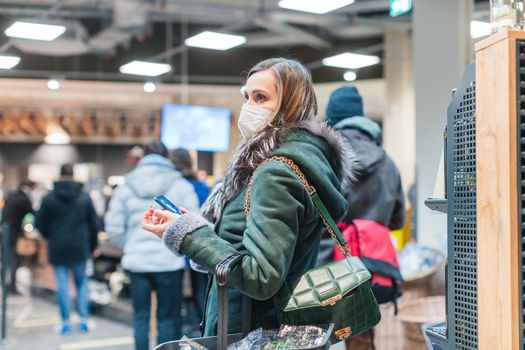 Woman standing in queue at cash desk in supermarket wearing mask