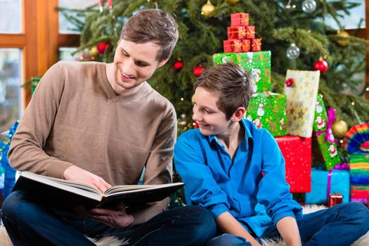Daddy reading out from book for kid under X-mas tree