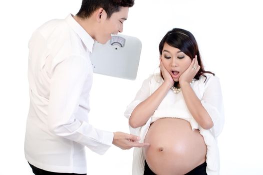 Man holding weigh scale pointing finger at his pregnant wife's belly