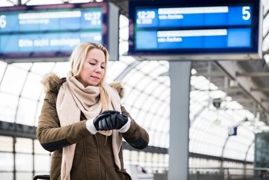 Woman looking at wristwatch in train station as her train has a delay
