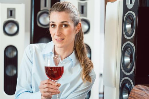 Woman having glass of wine in front of Hi-Fi speakers