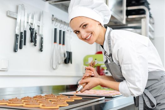 Confectioner woman using pastry bag to put cream on top of cookies