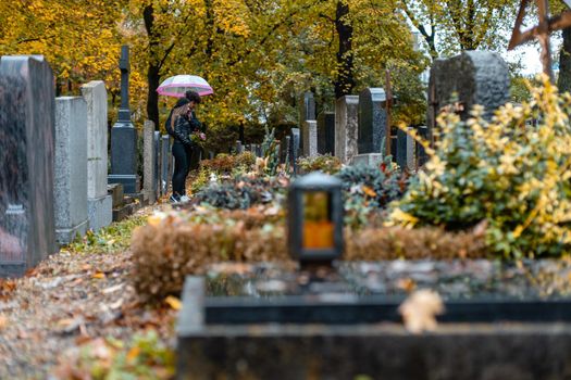 Graves on cemetery in autumn with a couple mourning the dead