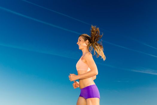Sport and Fitness - woman jogging under clear blue sky