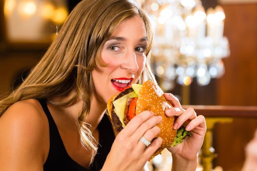 Young woman in fine restaurant, she eats a burger