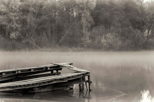 Old ruined pier on the river on a foggy morning.