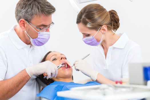 Female patient with dentist and assistant in a dental treatment, wearing masks and gloves
