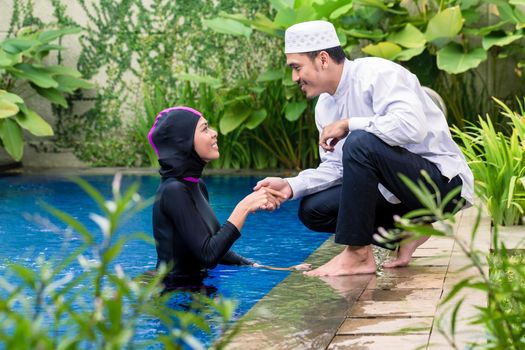 Muslim woman in pool greeting her husband