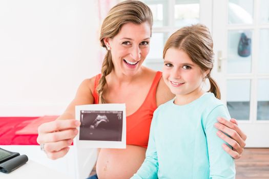 Expectant mother with sub-teenage daughter in her arm proudly presents ultrasonic scan