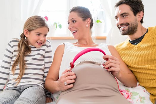 Family and pregnant mum using headphone on baby belly