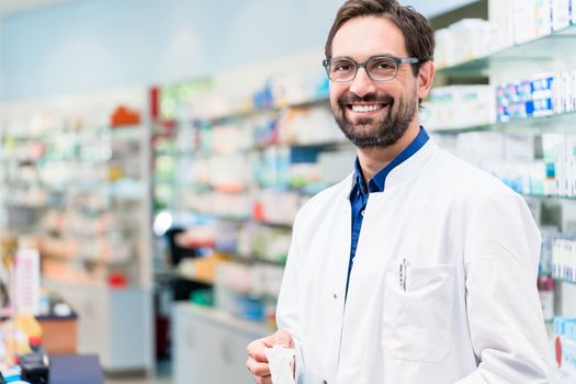 Apothecary in pharmacy standing at shelf with drugs