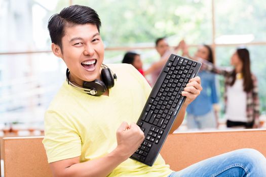 Young Chinese employee happy for his successful work on computer