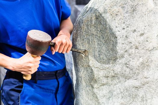 Stonemason working on boulder with sledgehammer and iron
