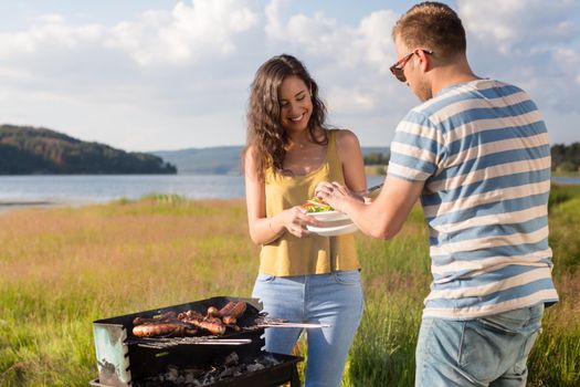 Man and woman having barbecue at lakeside in nature