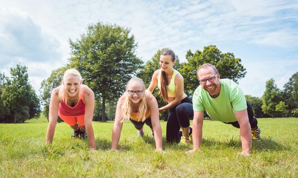 Family doing push-ups in nature under guidance by a fitness coach