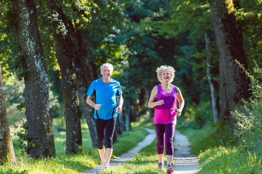 Two active seniors with a healthy lifestyle smiling while jogging