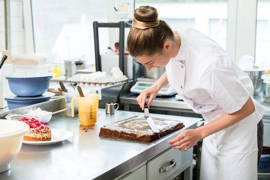 Confectioner woman getting chocolate cake ready with topping