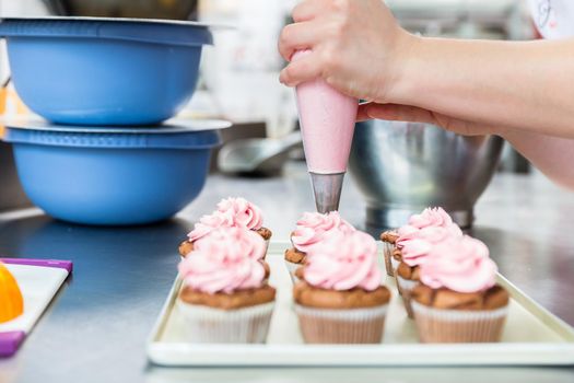 Women in pastry bakery as confectioner glazing muffins with icing