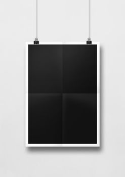 Black folded poster hanging on a white wall with clips